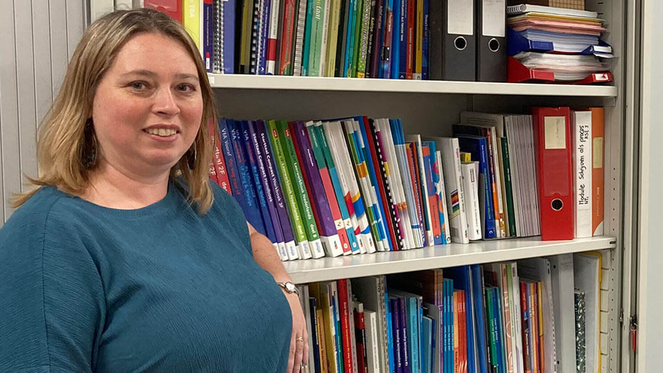 Taalcoördinator staand naast boekenkast