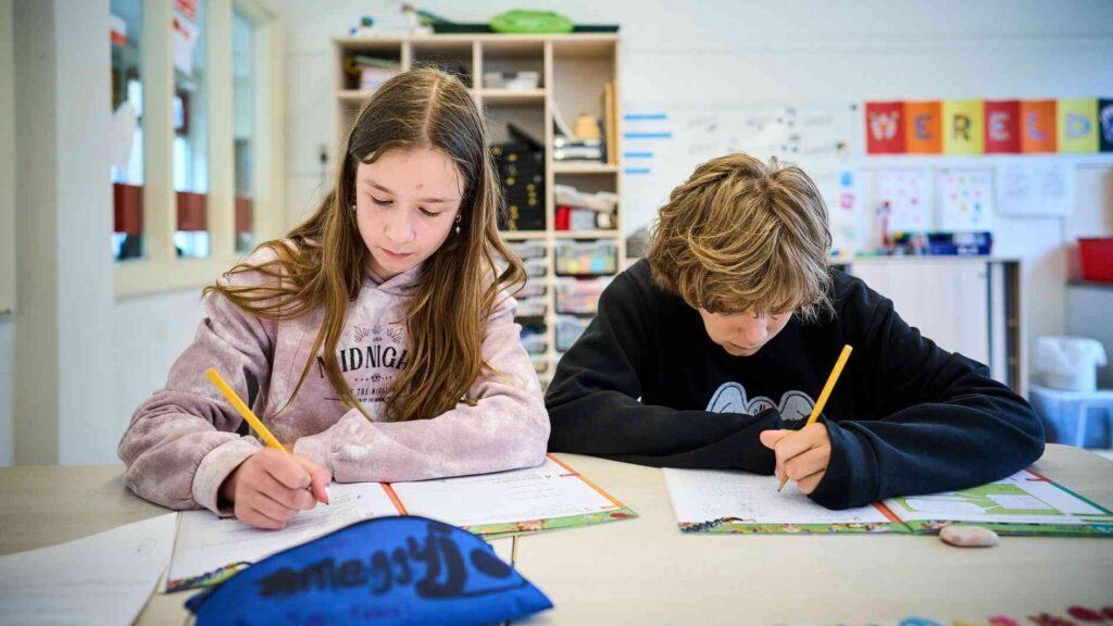een meisje en een jongen zitten naast elkaar in de klas en schrijven in hun schriften