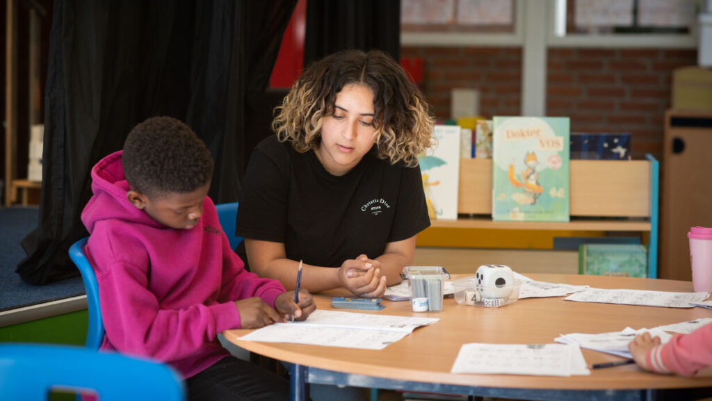 Een leerling en een leraar zitten in de klas aan de instructietafel