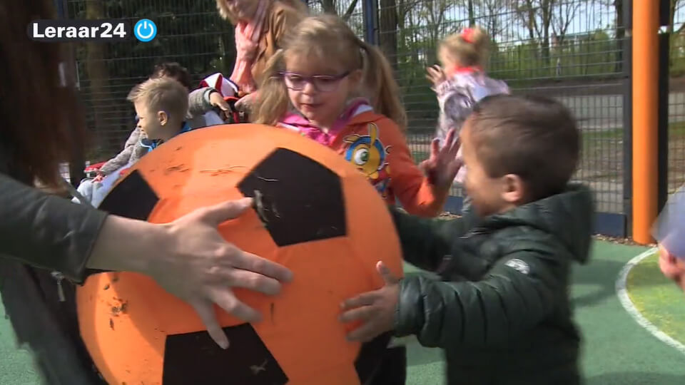 Kinderen geven een grote oranje bal aan elkaar door in het kader van de Koningspelen