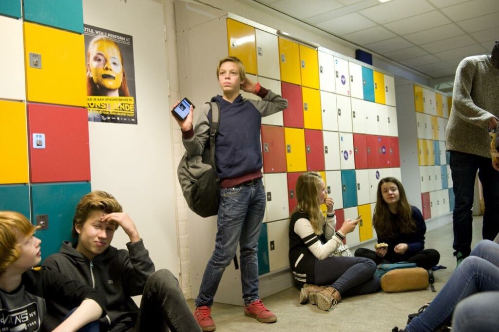 Leerlingen zitten en staan bij gekleurde kluisjes in een schoolgang. 