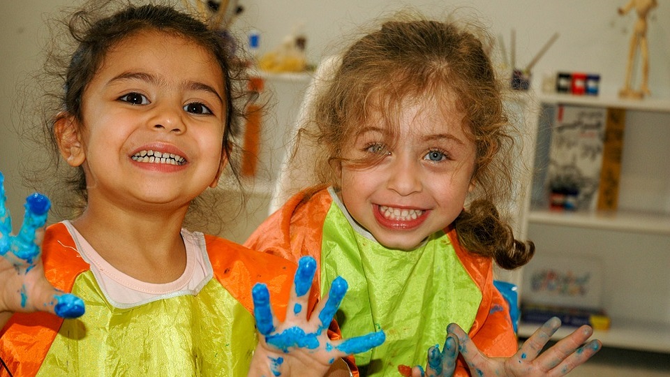 twee blije meisjes in de klas met verf aan hun vingers