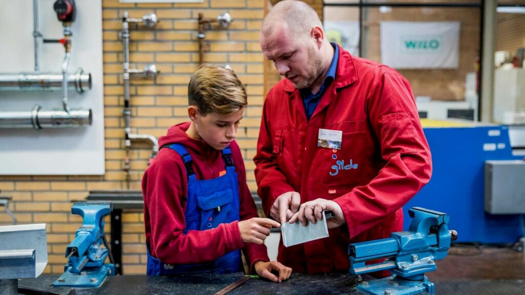 Docent en leerling beoordelen samen een zaagresultaat aan een werkbank